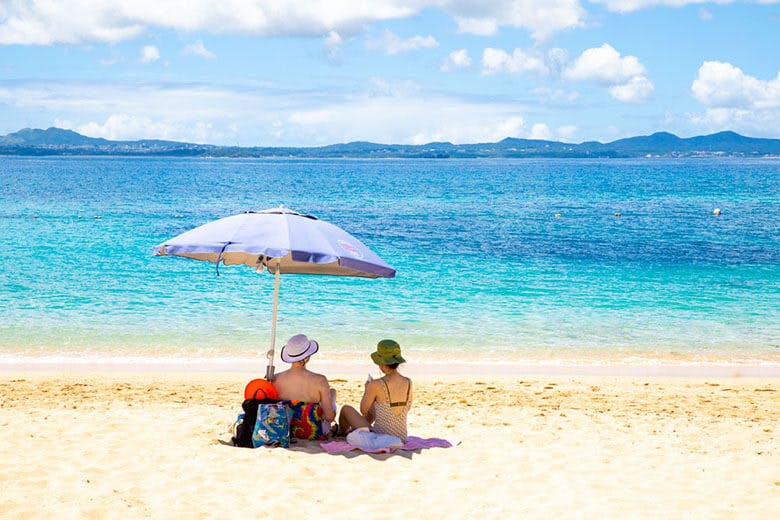 大泊(おおどまり)ビーチ|ビーチパラソルの下でくつろぐカップル越しに見える青い海