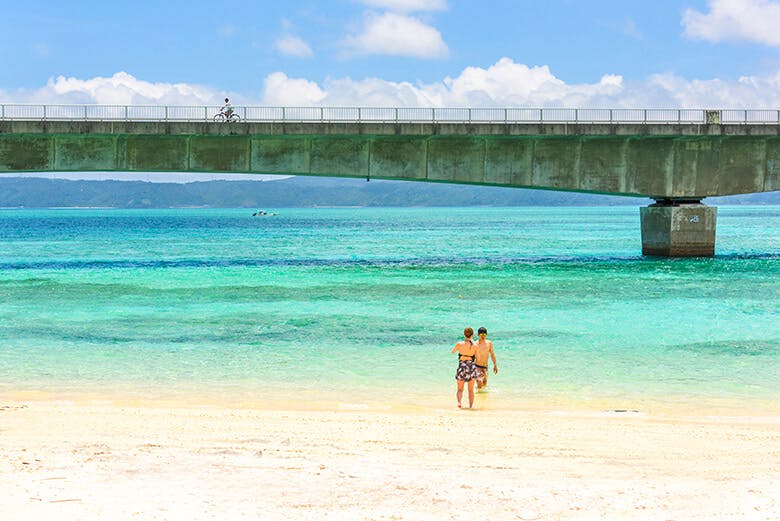 古宇利大橋|橋の下に広がる青い海とビーチで遊ぶカップル