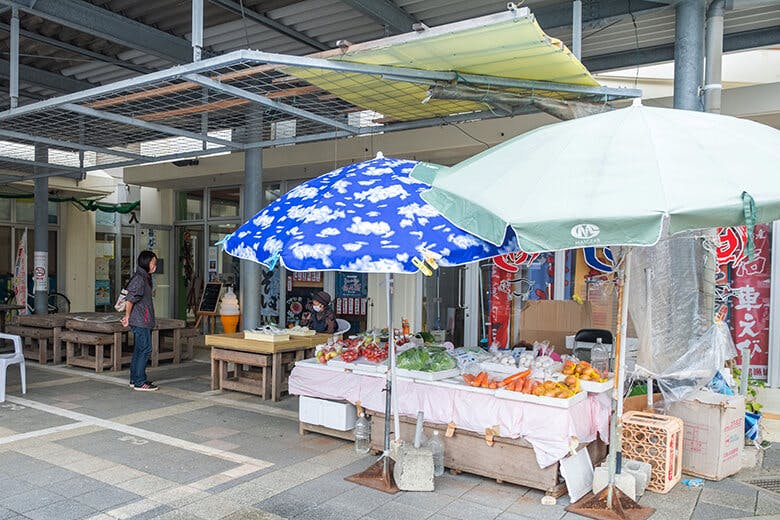 宮古島市公設市場｜パラソルの建てられた野菜売り場とおばぁ。