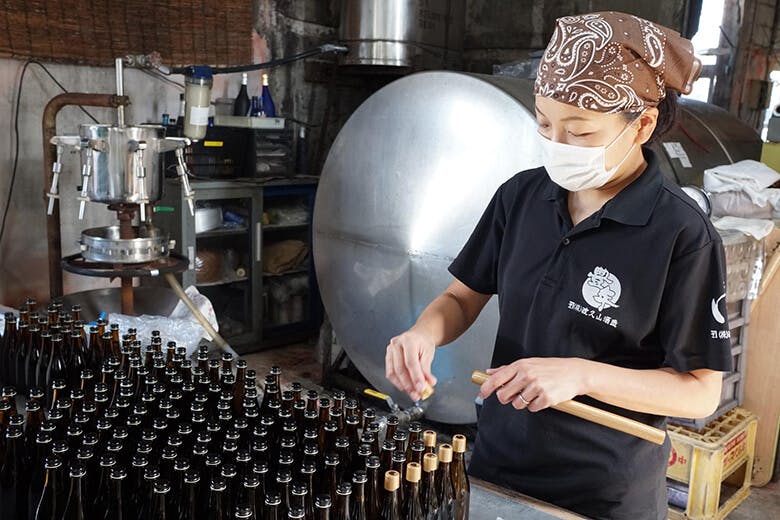 渡久山酒造|瓶詰めされた泡盛にフタをする女性