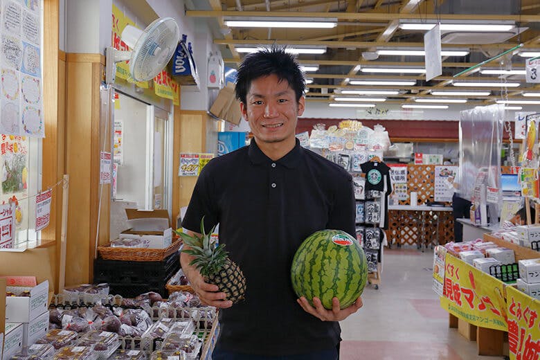 道の駅?豊崎|特産品のパイナップルとスイカをかかえる男性スタッフ