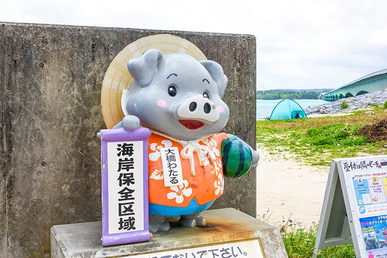 古宇利大橋|赤いアロハシャツに麦わら帽子をかぶり、左わきにスイカを抱えたグレーの豚のキャラクター像