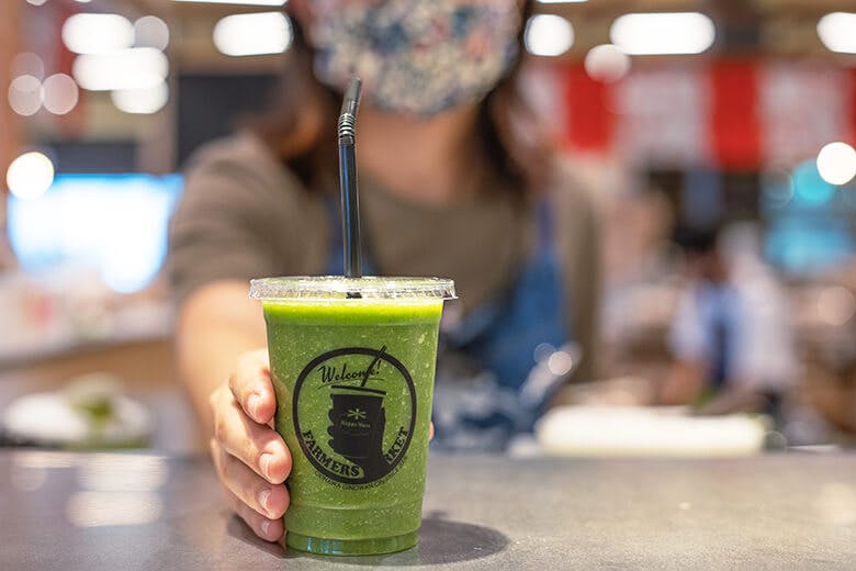 ハッピーモア市場|女性スタッフから差し出された緑色の鮮やかなスムージー