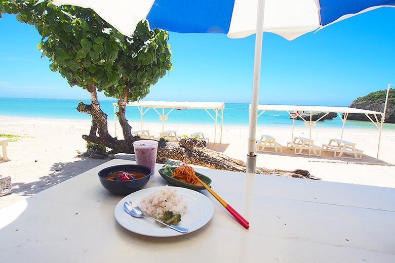 食堂かりか|ビーチパラソルの下にある真っ白なテーブルに並べられたお料理