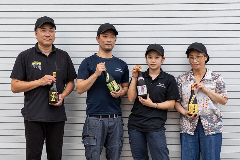 北谷長老酒造工場株式会社|商品の各種7合瓶を持ち構える、工場長の知念秀人さんとスタッフの皆さん