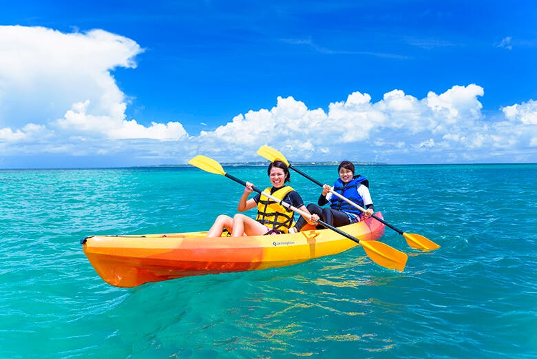 もとぶ元気村|青い海と空に映えるオレンジ色のカヌーに乗った女性たち