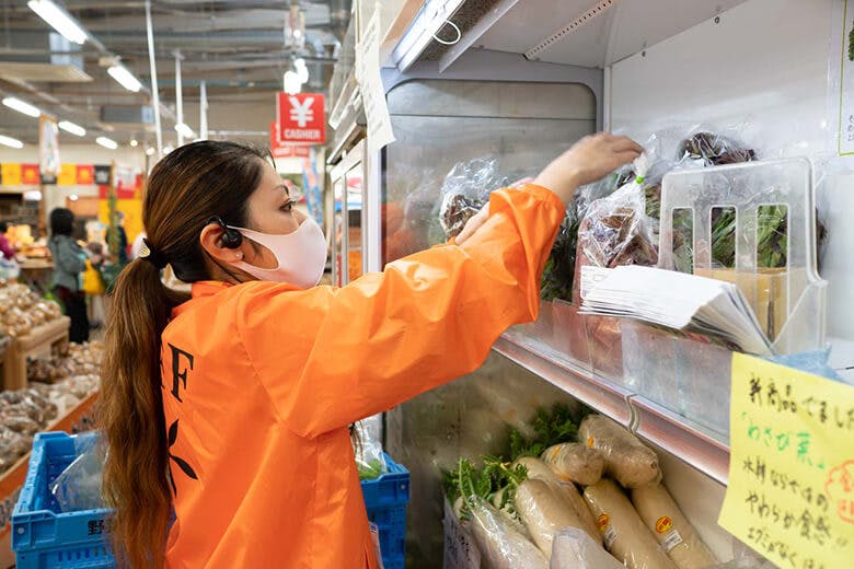 島の駅みやこ|商品を並べる、オレンジ色のユニフォームを着た若い女性スタッフ