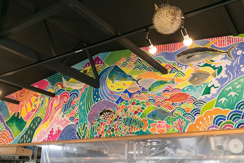 国頭港食堂（くにがみみなとしょくどう）｜カウンター上に飾られた、絵本作家savaが描いた、やんばるを表現したエネルギッシュな壁画