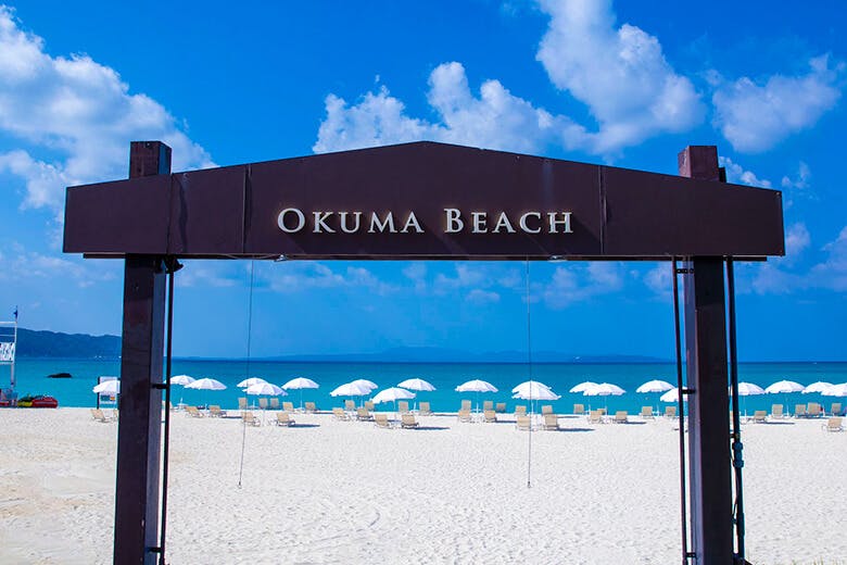 オクマビーチ|ビーチへのアーチと、抜けに見える青い水平線と白いパラソル群