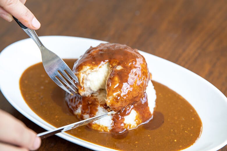 ばくばく亭|カレーに盛られたチーズインハンバーグにナイフを入れる様子