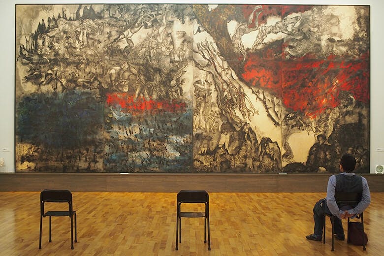 佐喜眞(さきま)美術館|黒と赤が象徴的な絵画と、その前の椅子に腰かけて鑑賞している男性